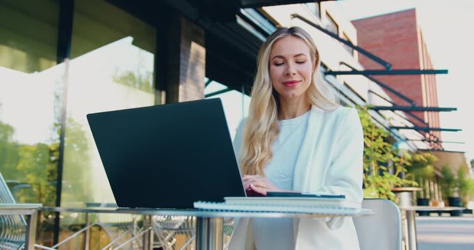 Professional businesswoman working remotely online on a tablet while sitting at a table outdoors.