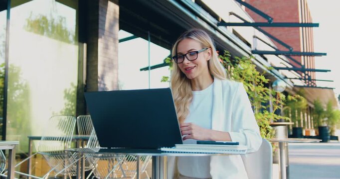 Professional businesswoman leading an online business meeting using a laptop while sitting at a table outdoors