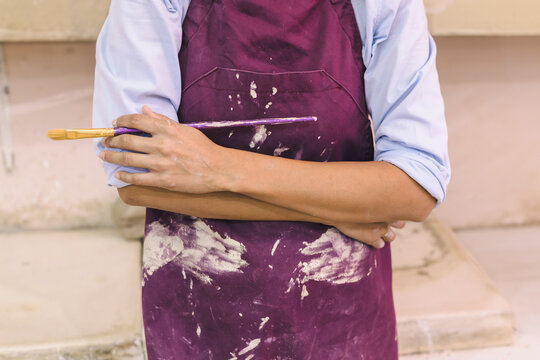 Mid section view of woman artist hands holds paint brushes, pottery artist, workshop. Ceramic art studio.