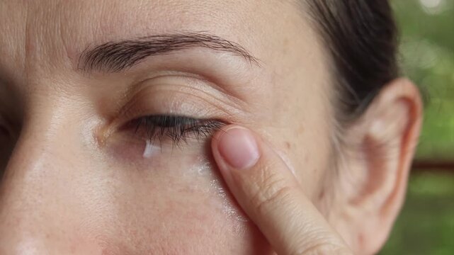 Middle aged woman applying eye cream with gentle massage. Close up of facial skincare around the eye area.  Wrinkles, anti aging care, hydration, beauty and daily self care. Real time footage concept