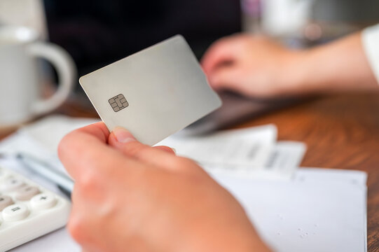 Person holding a credit card while reviewing bills and household expenses at a desk, representing personal finance, budgeting, debt management, banking, payments and financial planning