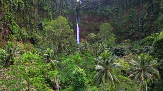 Aerial view of Kapas Biru Waterfall surrounded by lush tropical rainforest in East Java, Indonesia. Scenic jungle landscape with cascading water, mist, and vibrant green vegetation.