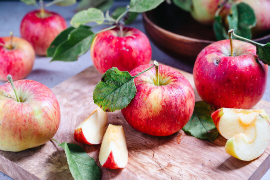 Fresh red apples with leaves and sliced pieces on wooden board