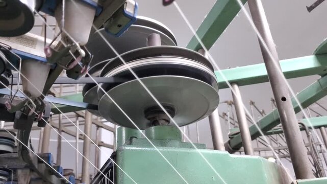 Circular Knitting Machine Yarn Feeder In Textile Factory Operation
Close up top view of a circular knitting machine's yarn feeding system in operation inside a textile factory. Multiple white yarn thr