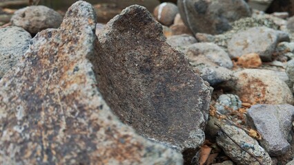 Weathered stone fragments lie scattered on pebbled ground. Texture and color detail highlight natural erosion and age. Rough surfaces contrast with smooth, rounded stones nearby © Rinz