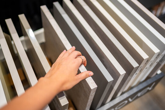 Woman touches countertop samples while choosing material in furniture showroom. Home renovation and interior design choice captured with selective focus and shallow depth of field