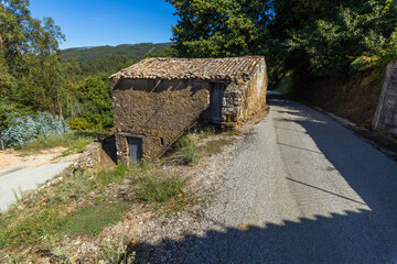 A rustic stone building stands beside a quiet asphalt road © wundermann