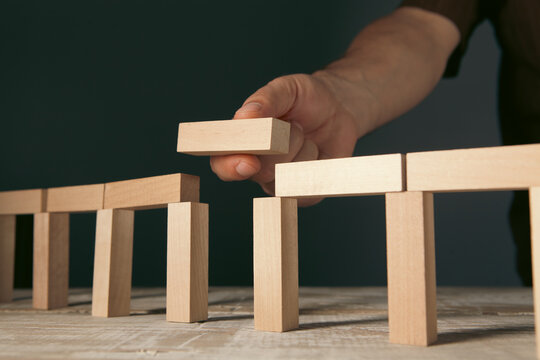 Constructing a toy bridge using wooden blocks and preparing to place the final piece in the gap to finish, concept