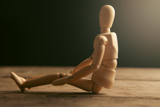 Wooden mannequin sitting on a wooden floor.