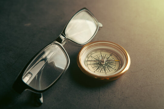 Compass and eyeglasses on grey background.
