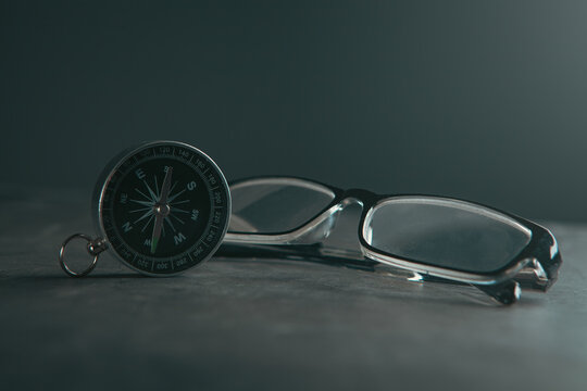 Compass and eyeglasses on grey background.
