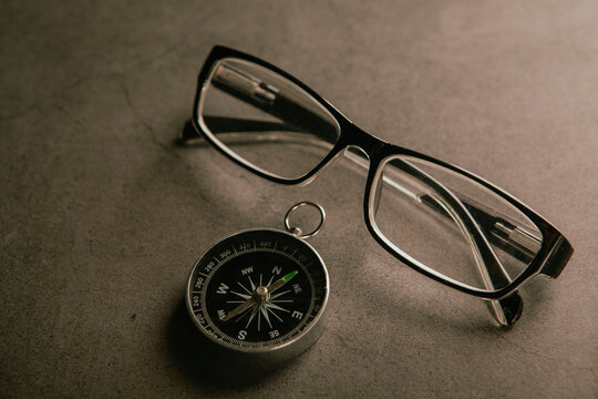 Compass and eyeglasses on grey background.