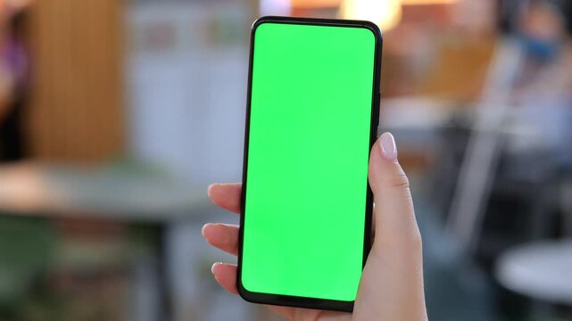 Hand holds smartphone with green screen. Background blurred indoor space. Three keyframes show same scene. Focus on phone screen