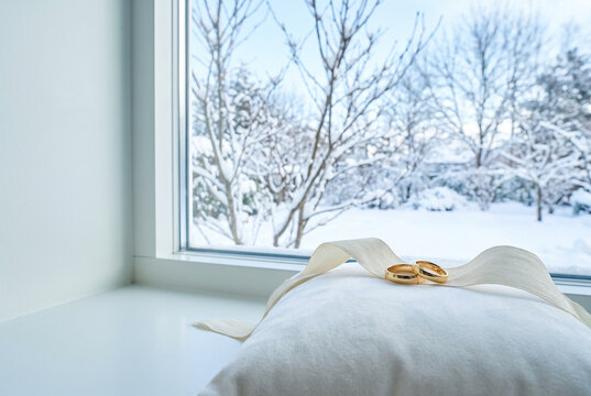 Wedding rings placed on a pillow by a snowy window  