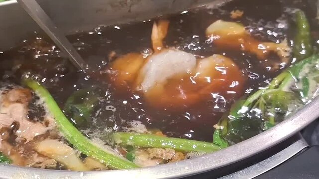 Fresh raw prawns being dipped and cooked in boiling hot soup ladled during Asian shabu shabu hot pot meal
