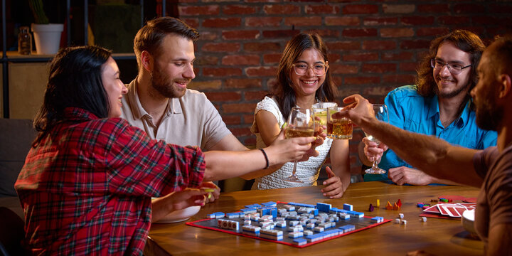 Friends clink glasses above Mahjong tiles during cheerful game night. Social celebration, friendship and indoor recreation concept.