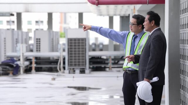 Engineer inspector in safety vest and hard hat performs industrial rooftop maintenance and building inspection, worker assessing wet ventilation equipment and pipes after rain