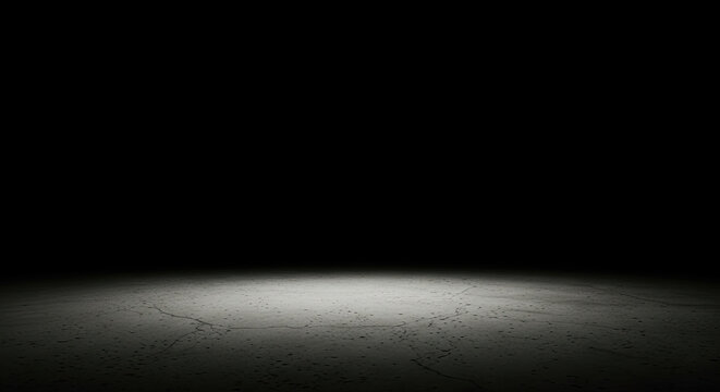 A bright spotlight illuminates a concrete floor, creating a stark contrast between the illuminated area and the surrounding darkness.