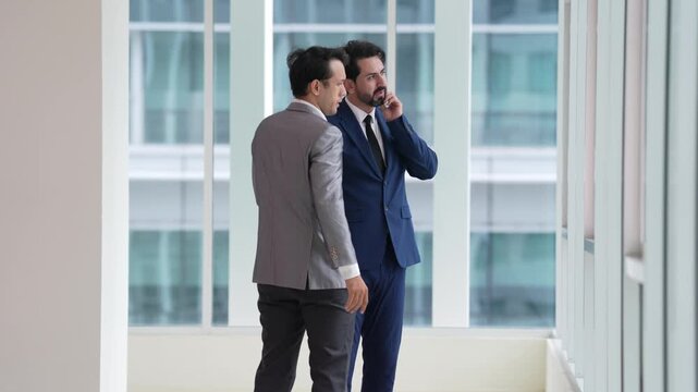 Businessman and colleague in suit hold office meeting near window, shifting from tense business conversation and workplace dispute to supportive professional worker hug