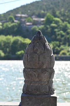 Carved Stone Finial by a Lake with Green Hillside Background