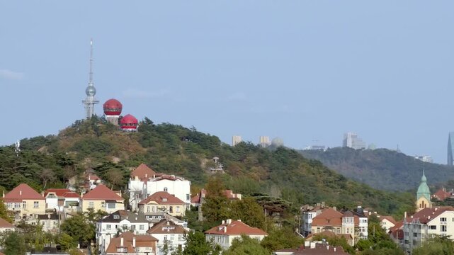 A hilly landscape features residential buildings and a tower with red domes under a clear blue sky.