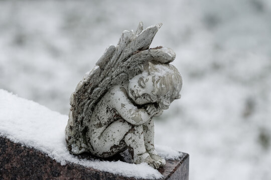 A small white angel grave ornament atop a headstone on a winter day. By November, the ground had already received a light covering of snow. 