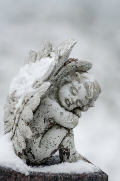 A small white angel grave ornament atop a headstone on a winter day. By November, the ground had already received a light covering of snow. 