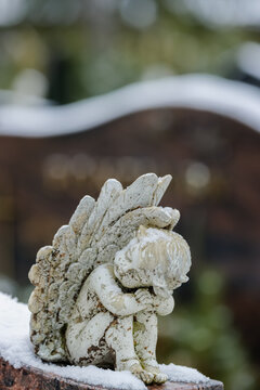 A small white angel grave ornament atop a headstone on a winter day. By November, the ground had already received a light covering of snow. 