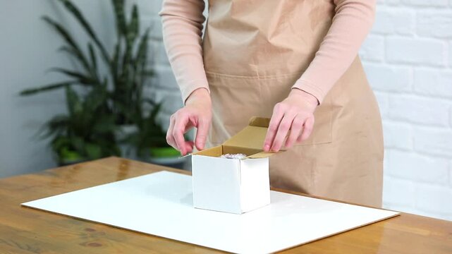 Woman unboxing ceramic vase from cardboard box, removing bubble wrap packaging at table. Online shopping parcel delivery, e commerce fragile item unpacking