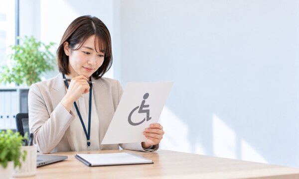 オフィスで車椅子マークの案内資料を確認しながらバリアフリー対応について検討する日本人女性