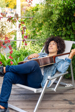 Beautiful young Afro-Italian mixed race man in casual wear playing guitar in the garden. A multiracial boy plays a musical instrument rests and relaxes outdoors. Spending time at home