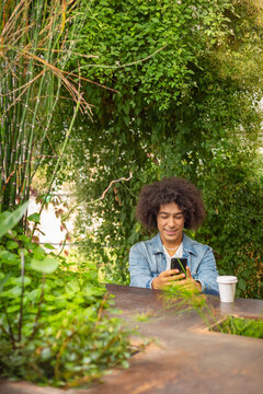 Smiling young ethnic guy 20 years old, dressed in casual clothes, works on a laptop outdoors, in a green area in nature. Green open space for coworking, freelancer, relaxing, coffee, food. Free place