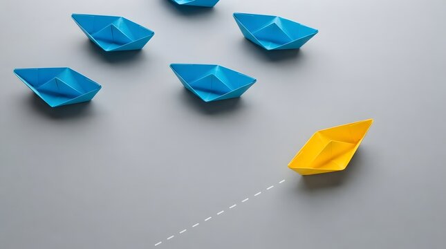 Yellow paper boat sailing ahead of blue paper boats on grey surface with standing out