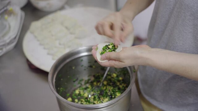 A person places dumpling filling onto a dough wrapper while preparing homemade dumplings in a kitchen.