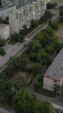 Aerial view of apartment blocks with greenery and roads. Buildings stand tall, surrounded by trees and parked cars. View captures daily urban life from above, calm and unbothered