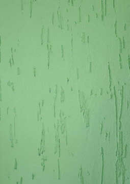 Close up of a light green textured wall with stucco or scraped paint finish, showing vertical diagonal lines and raised bumps. Organic distressed surface ideal as a background.