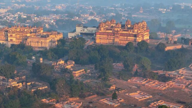 Cinematic drone orbit revealing historic Jahangir Mahal and Raja Mahal amid the wooded landscape and historic architecture of Orchha.