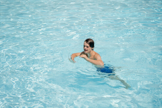 Teenage boy with Down syndrome swimming independently across spacious outdoor pool in summer