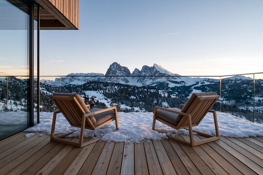 Luxury wooden balcony with lounge chairs overlooking snowy mountain peaks