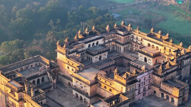 Cinematic drone orbit around historic Raja Mahal in Orchha, revealing its ornate Bundela-era architecture, courtyards, arches, terraces and surrounding greenery in Madhya Pradesh, India.