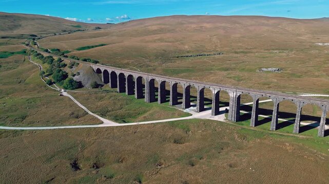 Ancient stone bridge stretches across rolling green hills. Ribblehead Viaduct is a majestic 19th-century railway bridge