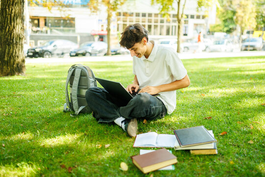 Attentive caucasian student typing on a laptop on the green outdoor lawn.