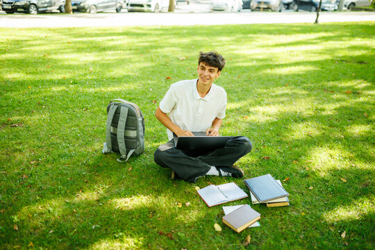 Smiling caucasian student taking a break from his laptop on the park grass.