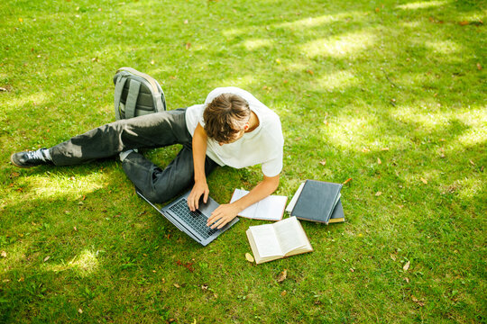 Top Down View Of A Caucasian Student Typing On A Laptop Outdoors.