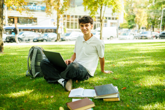 Smiling Caucasian Student Taking A Laptop Break On The Campus Grass.