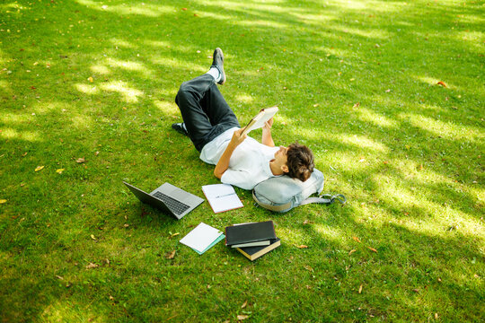 Top down view of a relaxed student reading a book on the campus grass.