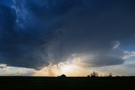 Farm house with storm clouds and sun rays at Sunset in alberta, Canada