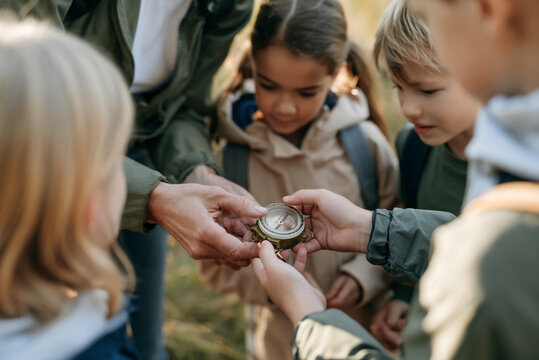 Teacher showing children how to use compass during autumn school hike, focus on student's hands holding compass, practical education concept.