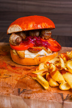 Gourmet loaded burger with meatballs, tomato slices, caramelized red onions, melted cheese and roasted potato wedges, served with seasoned fries on a rustic wooden board.