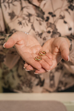 Close-up of a woman holding two small gold hoop earrings in her open hands, elegant jewelry and fashion accessory concept.